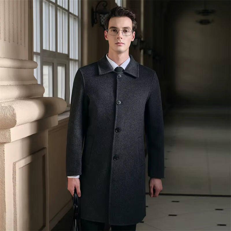 Male model wearing a dark gray men's pure wool slim fit overcoat with a classic collar, button closure, and tailored fit, standing indoors near a window