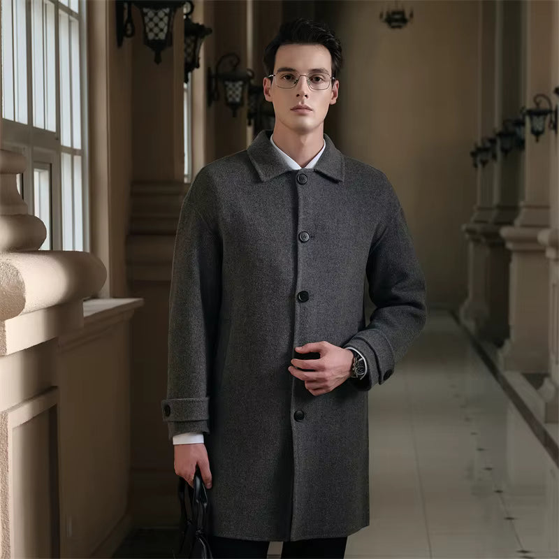 Men's slim fit overcoat in dark gray wool fabric, classic collar, button closure, worn by a young man in an elegant indoor setting
