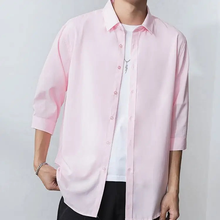 Julian's | Person wearing a light pink shirt over a white shirt with rolled-up sleeves on a plain background