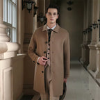 Male model in beige men's pure wool slim fit overcoat, layered over a shirt and tie, standing in an elegant, classic interior hallway.